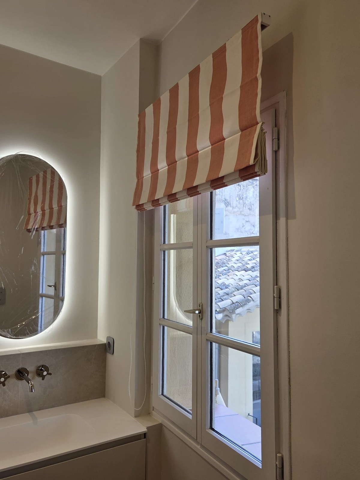 Salle d'eau avec miroir ovale rétroéclairé et store à rayures