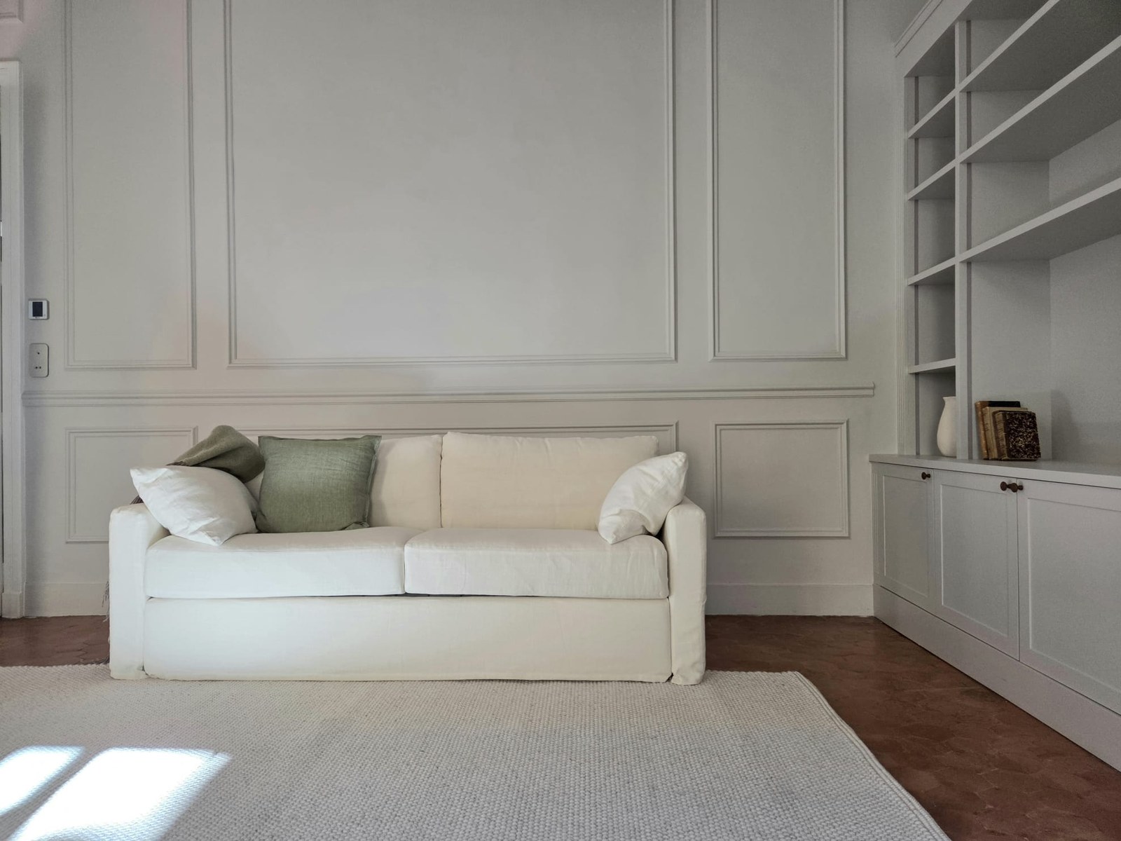 Salon aux boiseries blanches, canapé clair et bibliothèques sur mesure