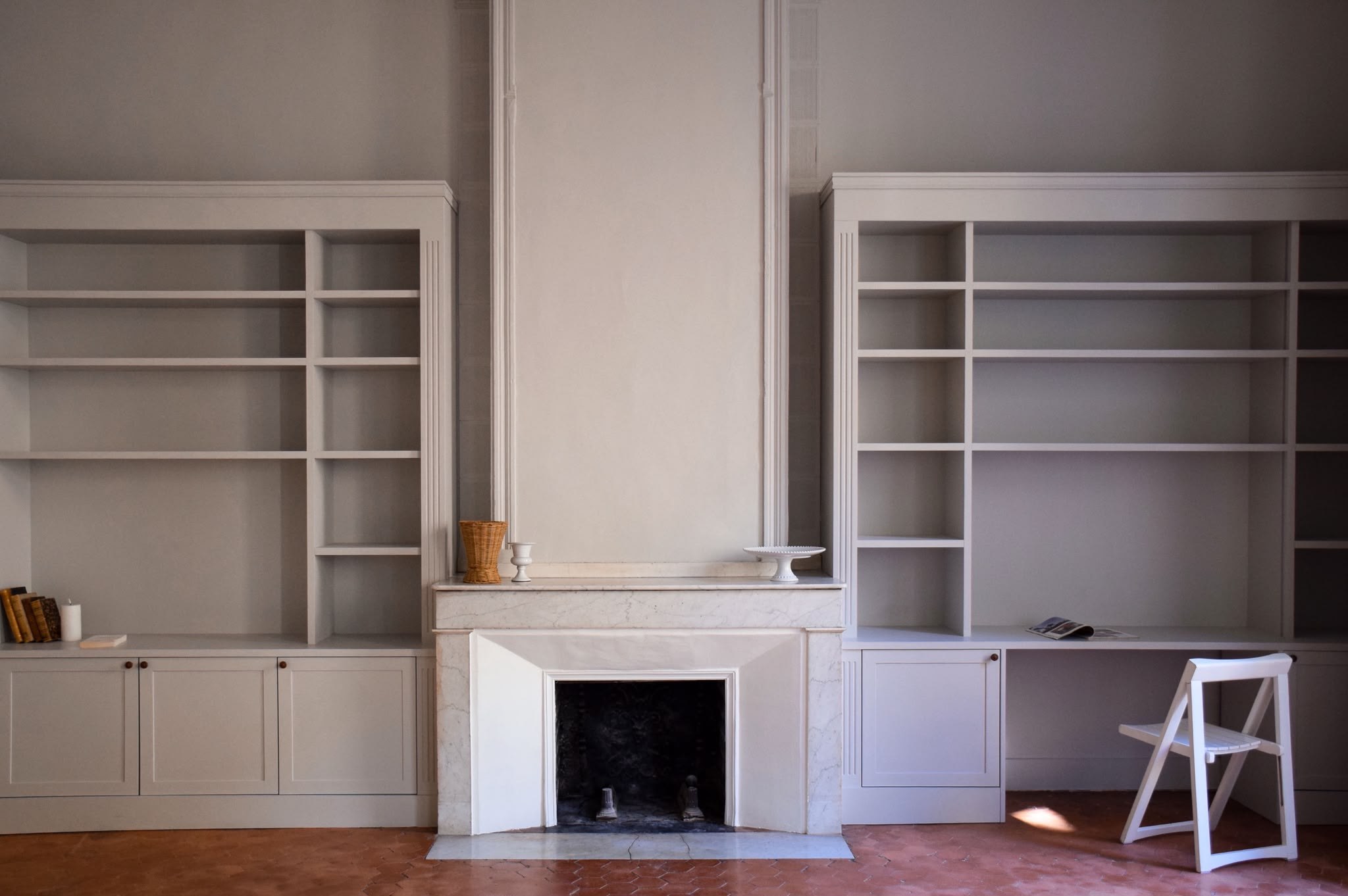 Cheminée en marbre blanc entre deux bibliothèques sur mesure peintes en gris, sol en tomettes